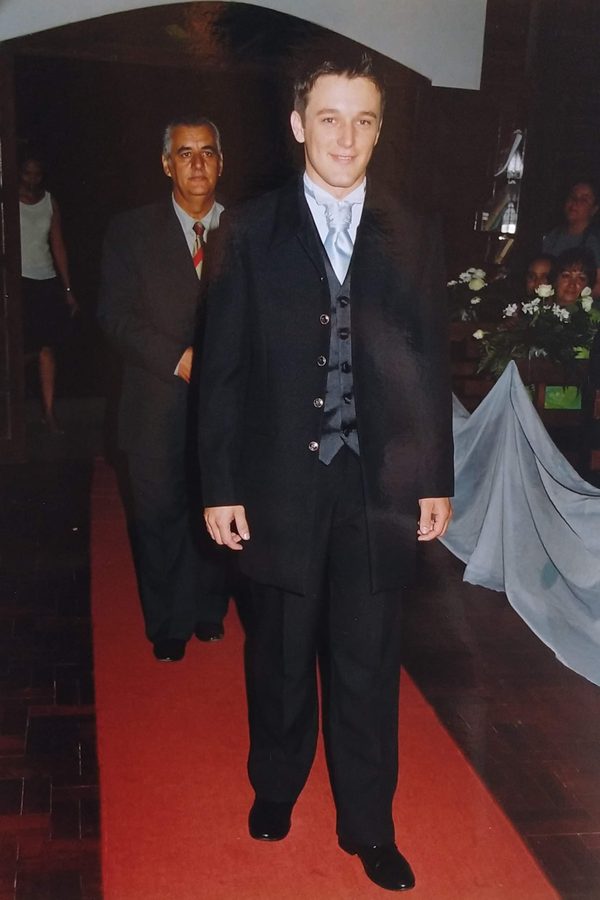 Jovem de terno em um tapete vermelho, com um homem mais velho ao fundo