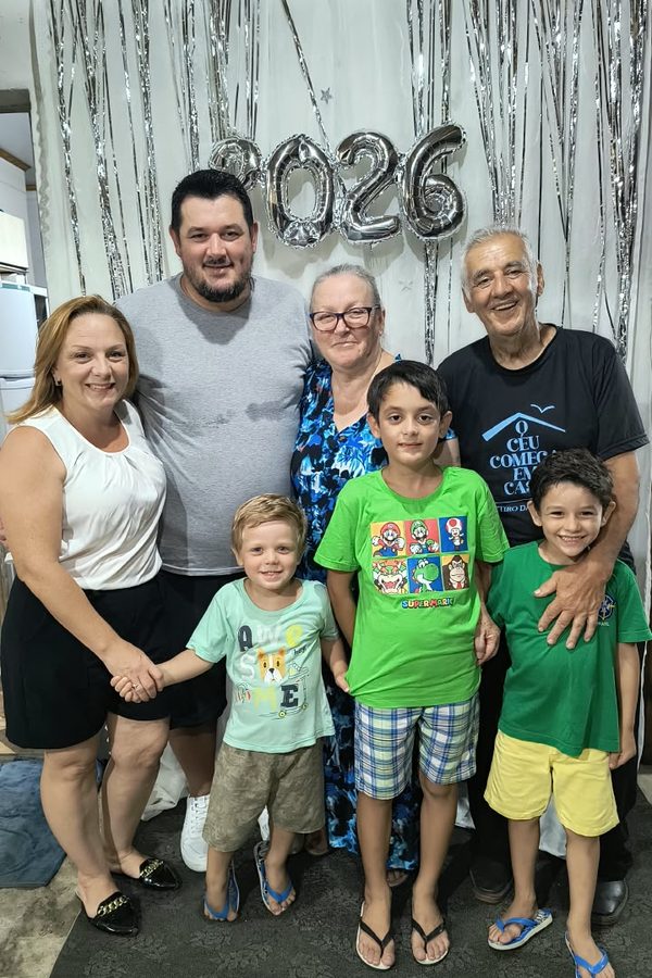Família em pé, com crianças, diante de uma decoração prateada de 2026