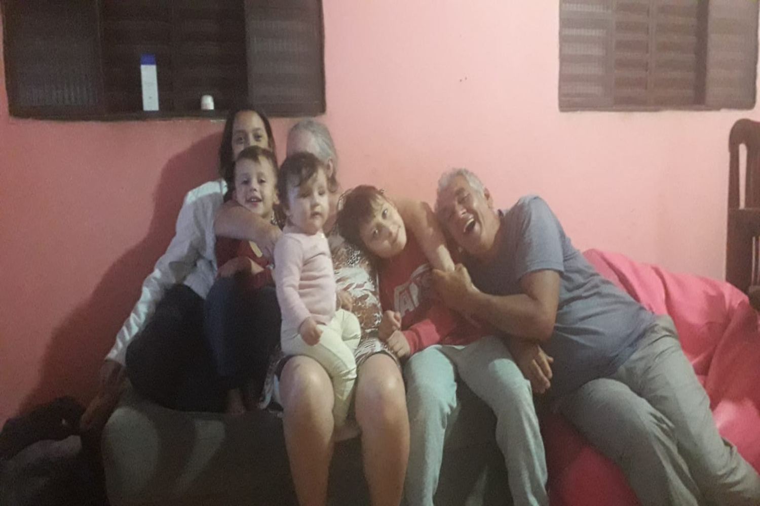 Sinval deitado no sofá, rindo, abraçado aos netos