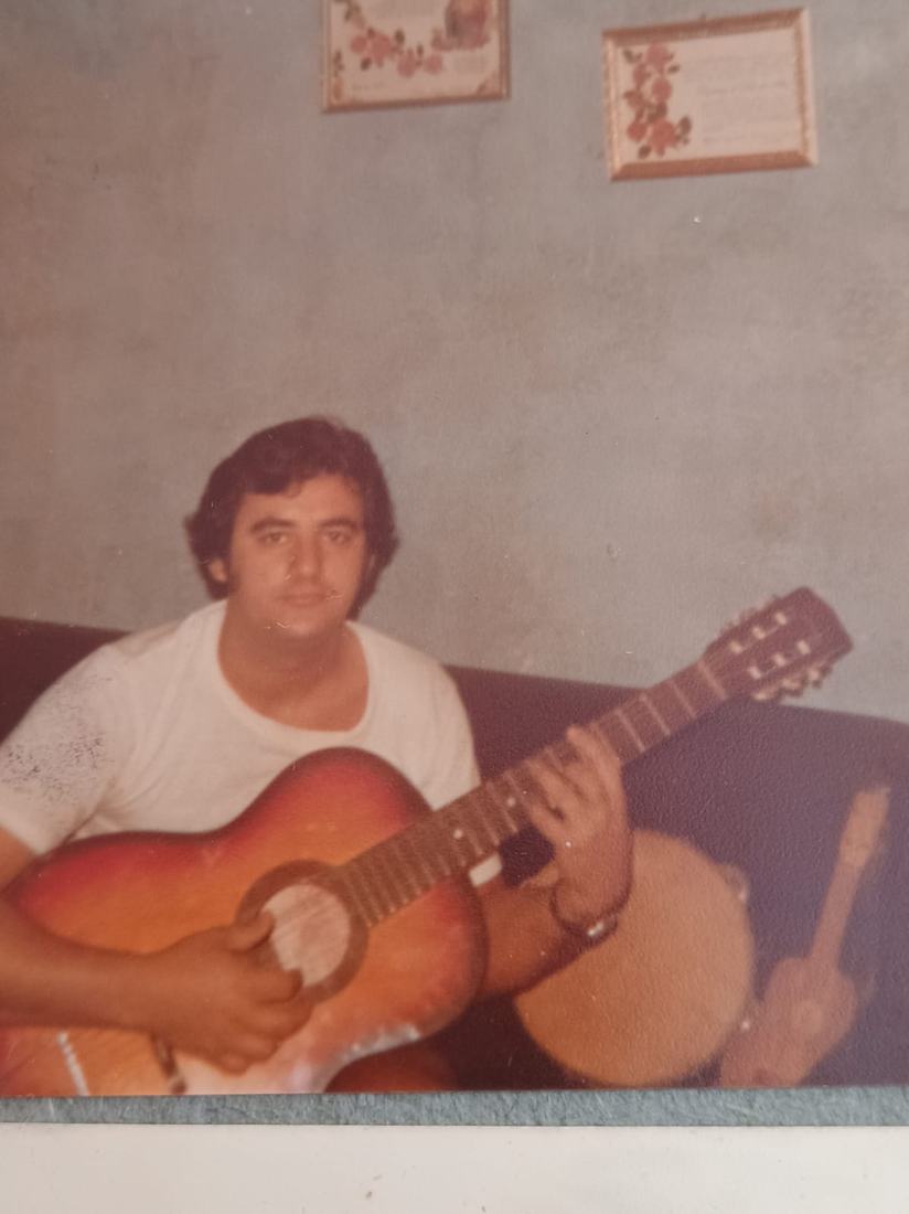 Fotografia antiga de um homem de camiseta branca tocando violão