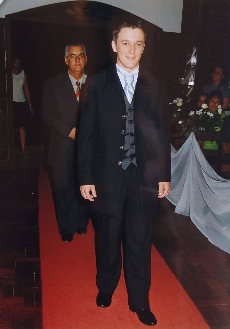 Jovem de terno em um tapete vermelho, com um homem mais velho ao fundo