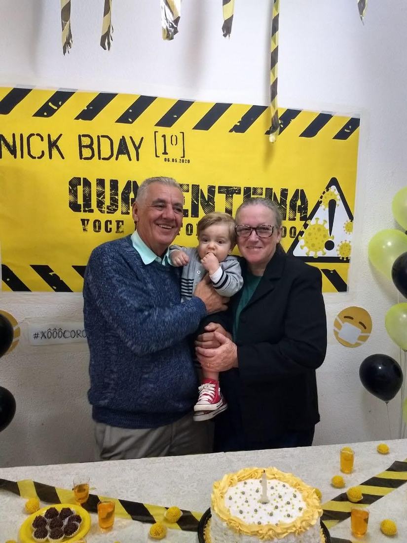 Um senhor segurando um bebê ao lado de uma mulher, em uma festa de aniversário