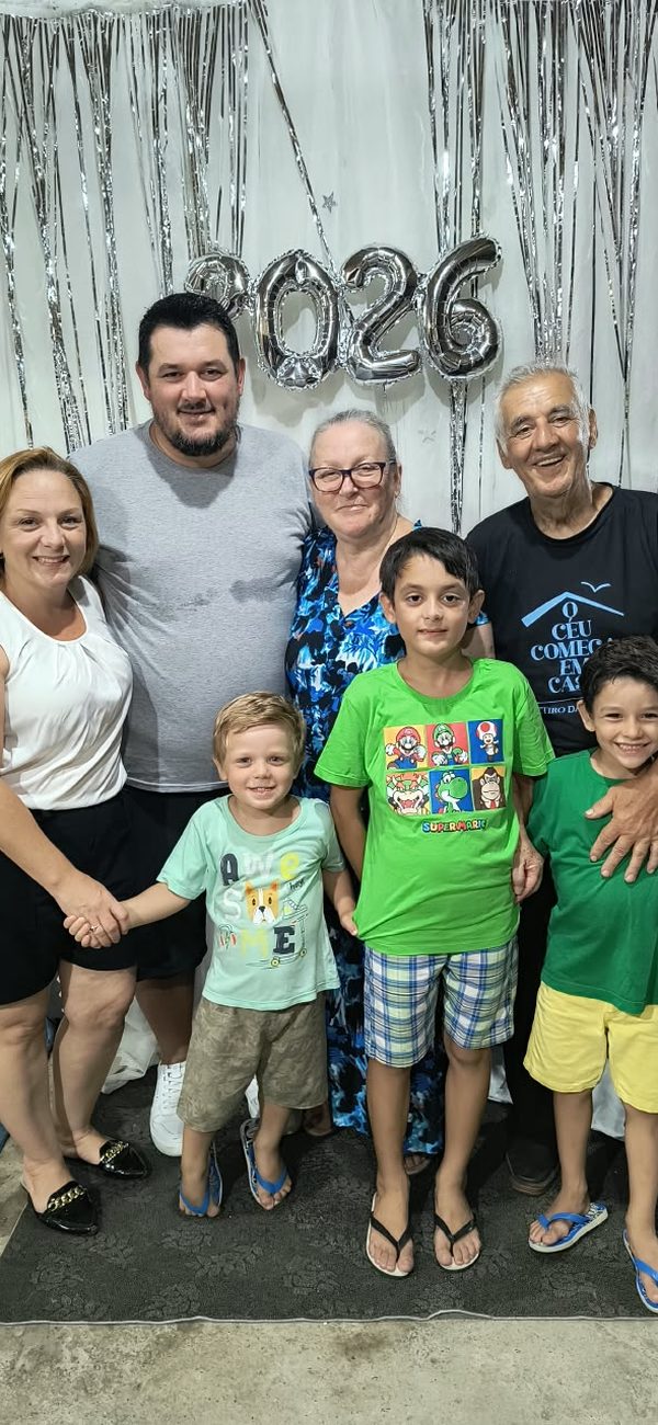 Família em pé, com crianças, diante de uma decoração prateada de 2026