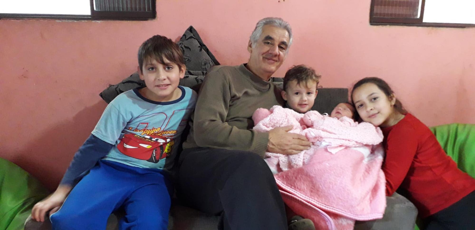 Sinval sentado no sofá com os netos e um bebê recém-nascido