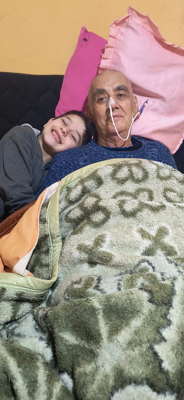 Sinval deitado, sorrindo ao lado de um neto abraçado a ele