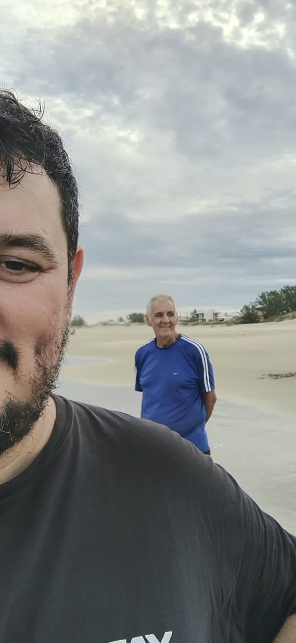 Selfie de um rapaz com Sinval ao fundo, numa praia