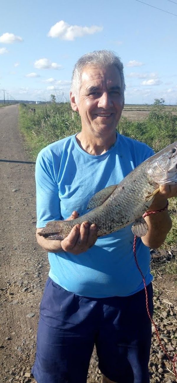 Sinval sorrindo, segurando um peixe numa estrada de terra