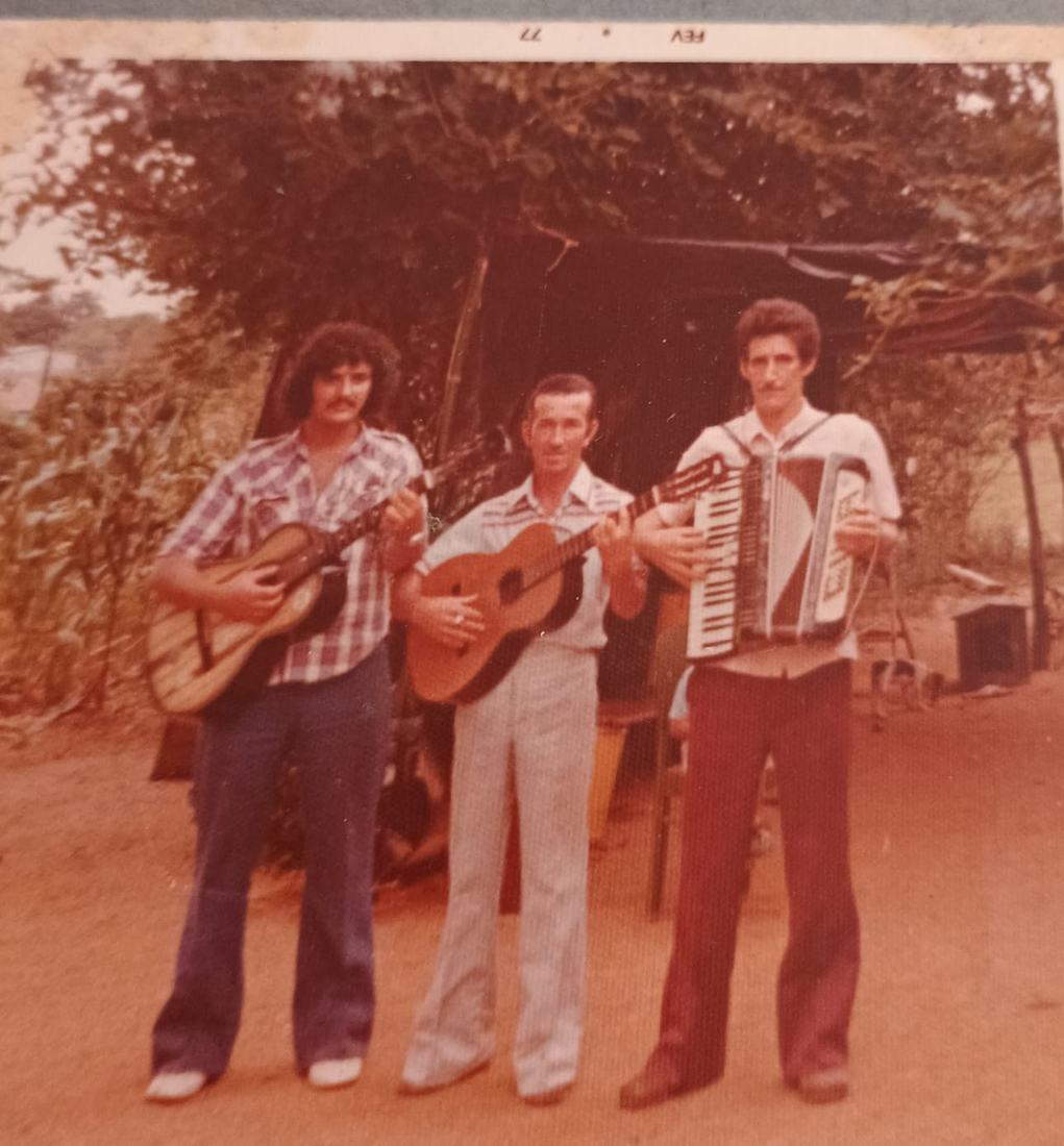 Três homens tocando instrumentos ao ar livre, em fotografia antiga