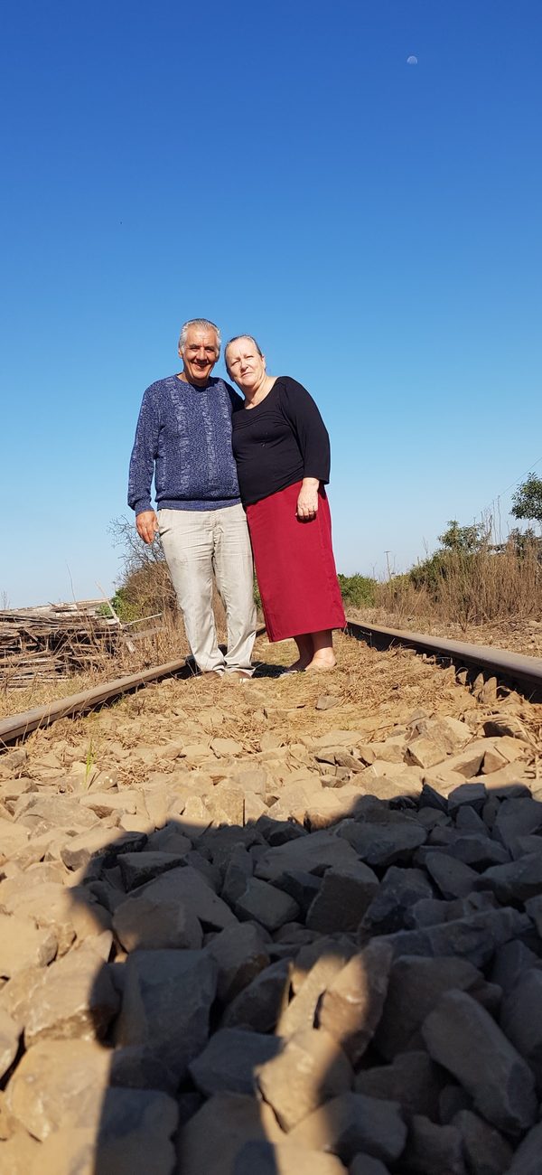 Casal abraçado sobre os trilhos de um trem, sob céu azul