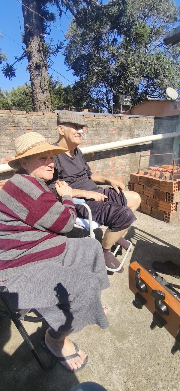 Casal de idosos sentados ao sol, vistos de costas