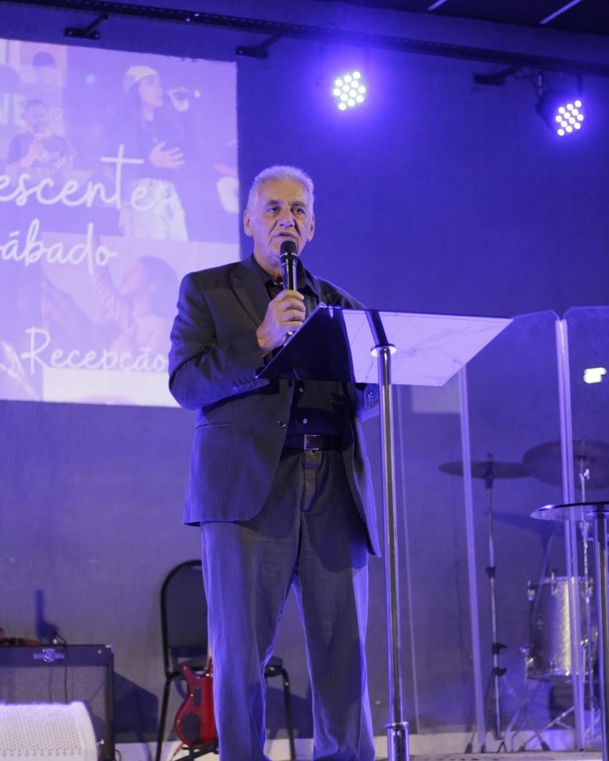 Sinval pregando com o microfone, em um palco iluminado