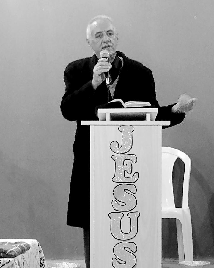 Sinval com o microfone junto a um púlpito com a palavra Jesus